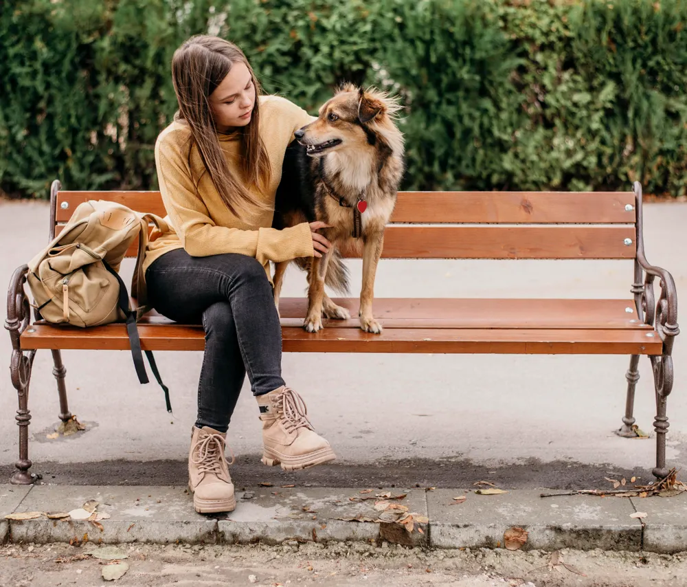 A girl sitting with a dog on a bench.