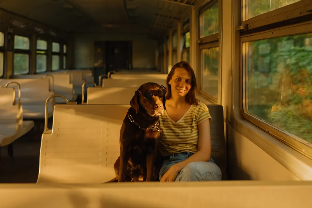 A woman wearing glasses sitting with her dog on the train.
